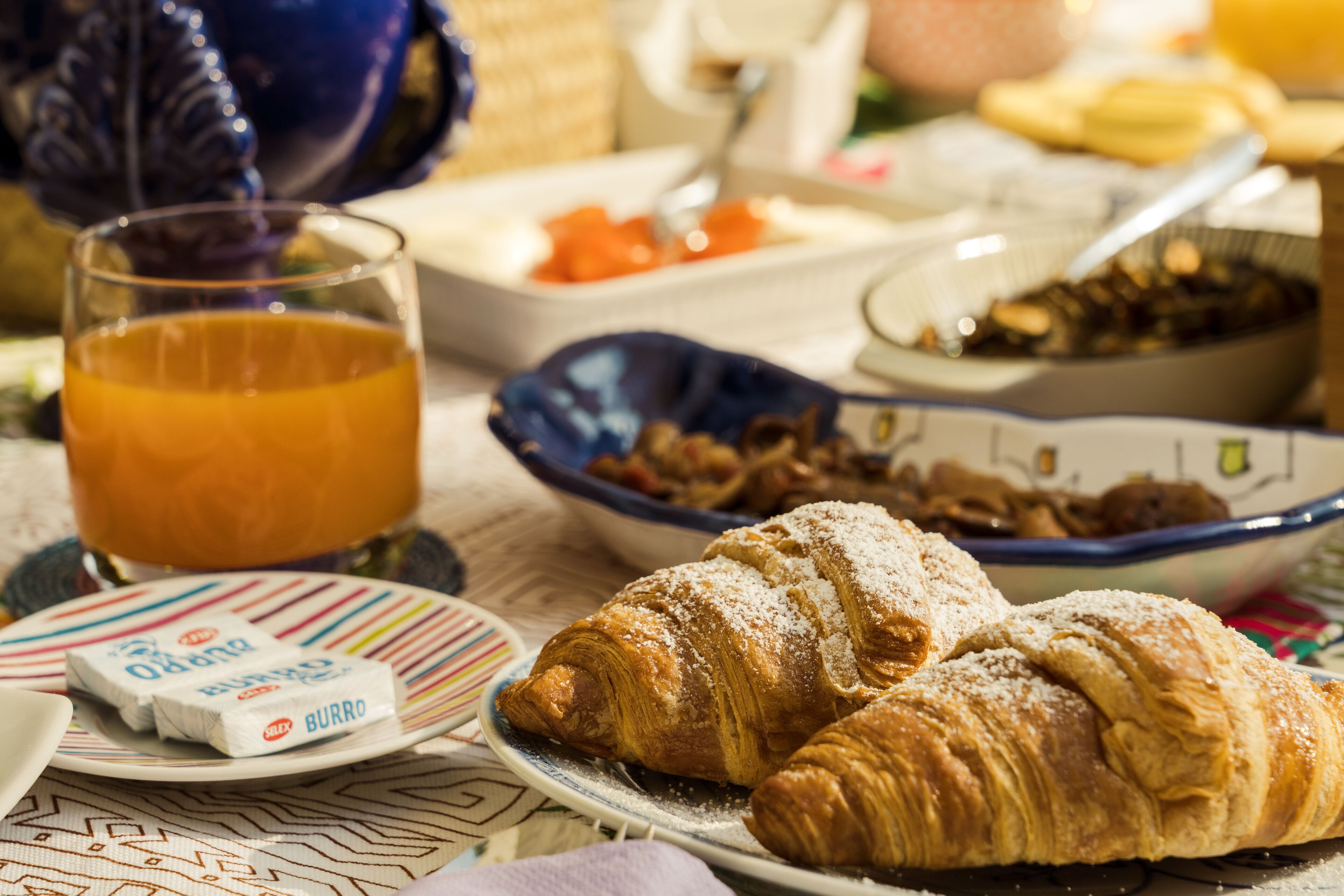 A breakfast setting with croissants, a glass of orange juice, and various breakfast items on a table.