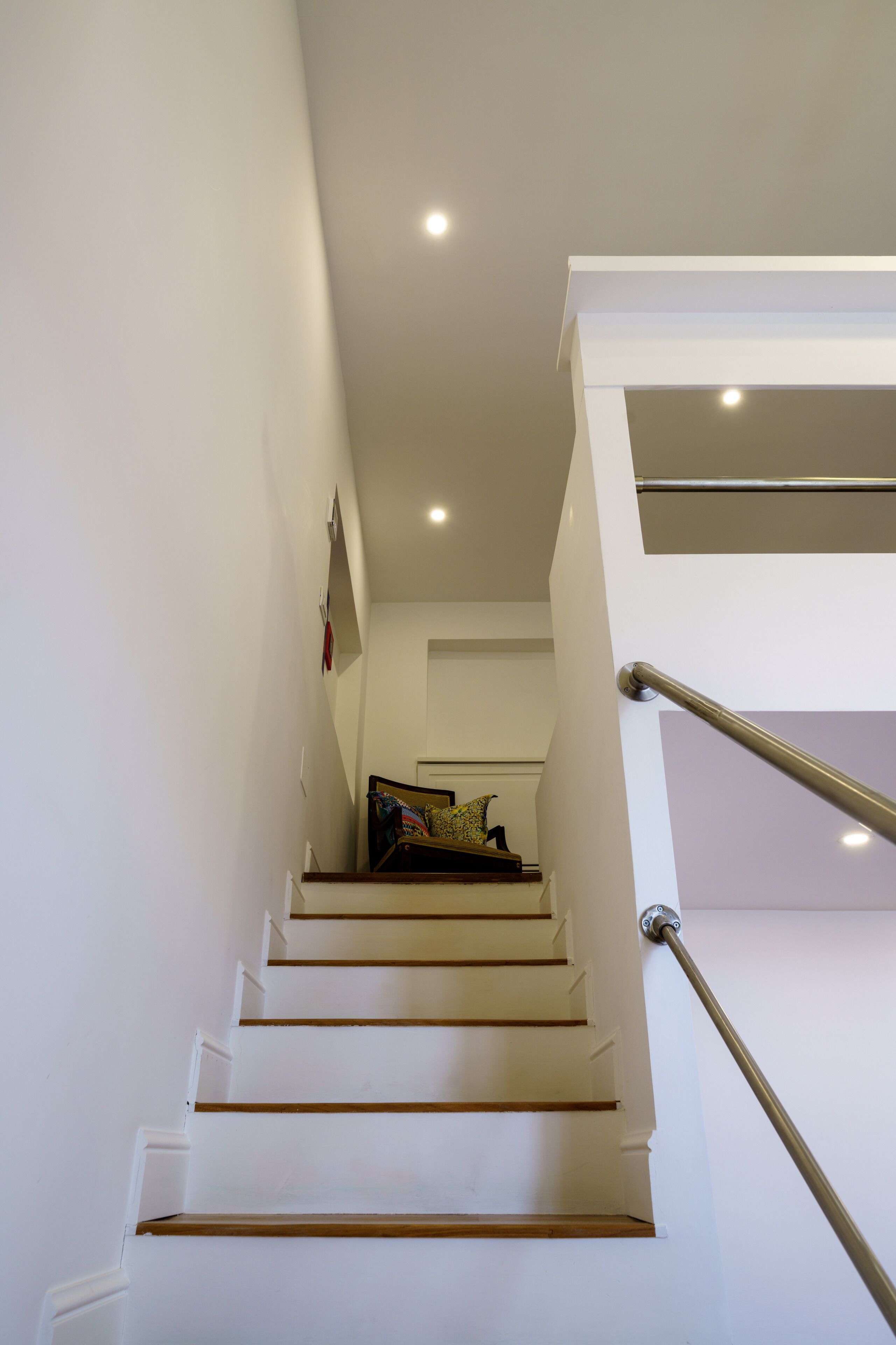 A staircase with white walls and a metal handrail leading to a landing.