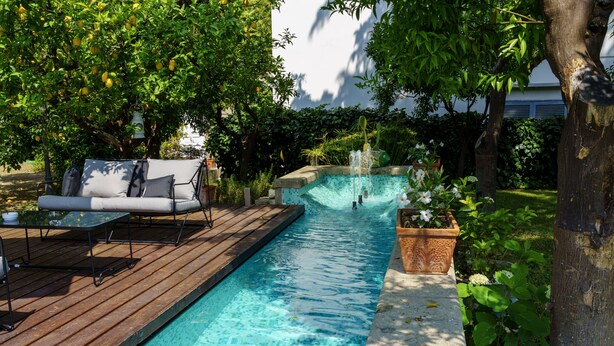 Una piscina con cubierta de madera, un área de descanso con sofá y mesa, y una fuente de agua.