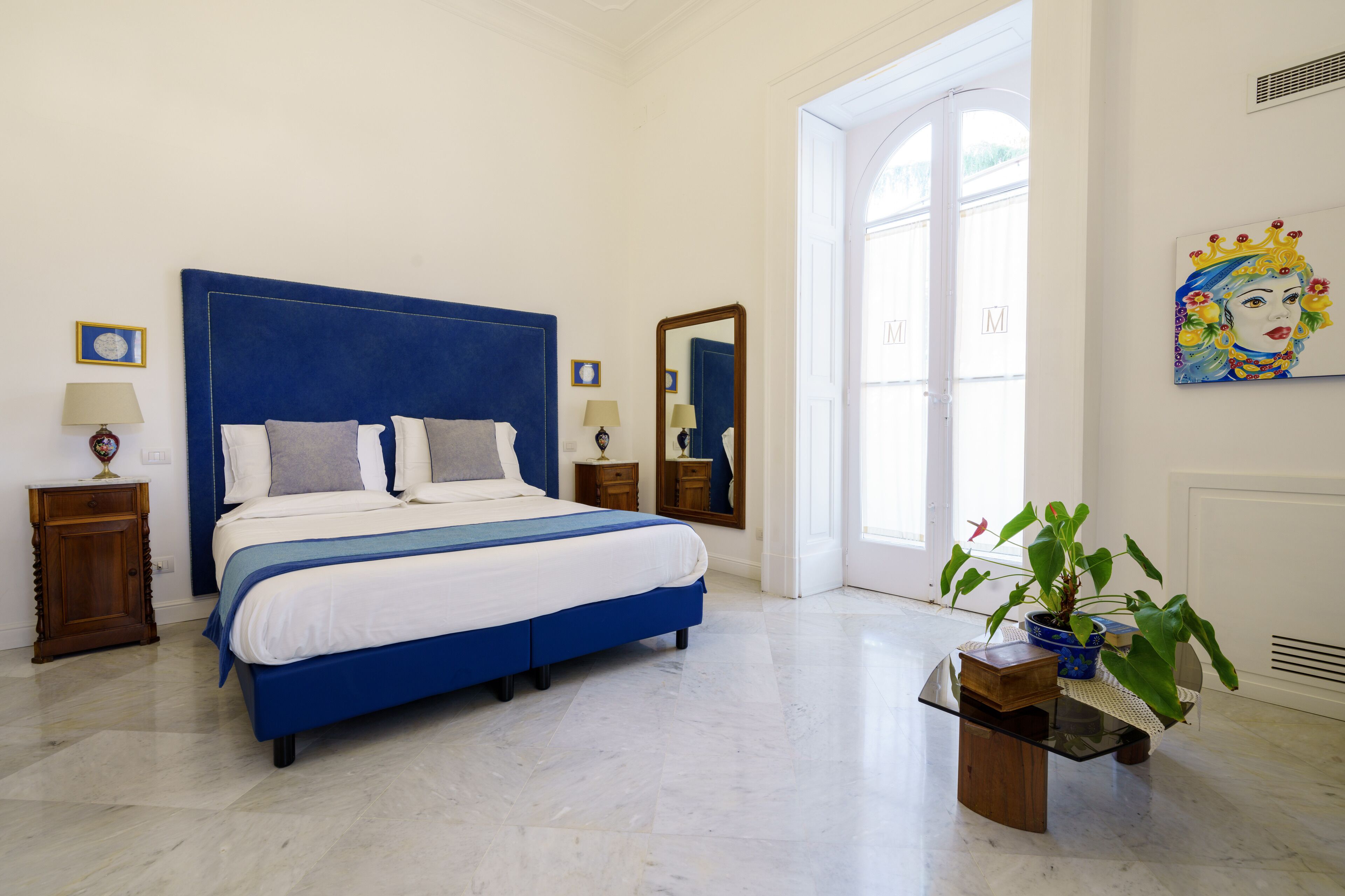 Une chambre avec un grand lit, des tables de chevet, un miroir, une fenêtre et une plante en pot.