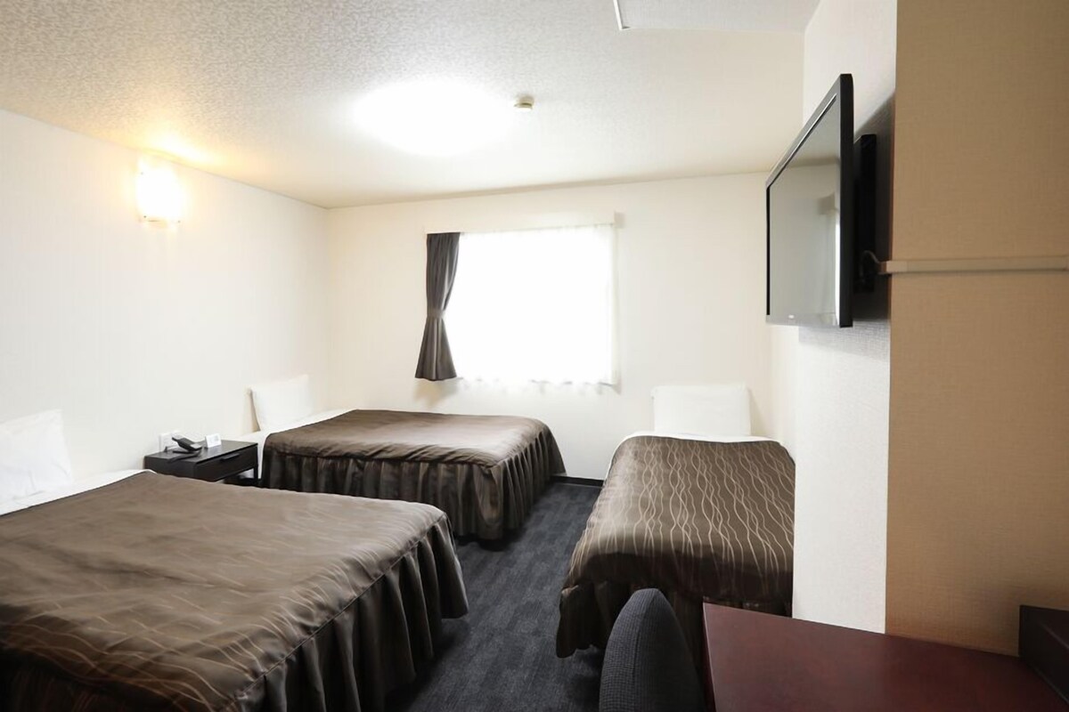 A hotel room with two beds, a desk, a chair, a TV, and a window with curtains.