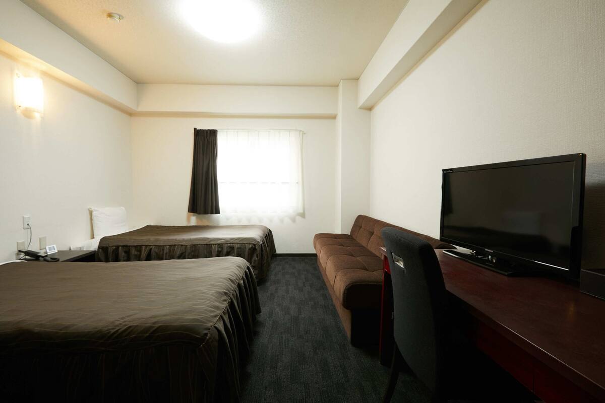A hotel room with two beds, a sofa, a TV, and a desk.