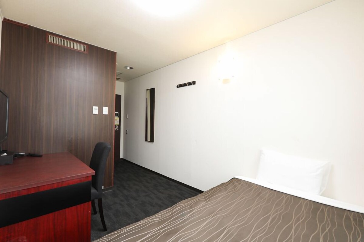 A hotel room with a desk, a chair, a bed, and a wall-mounted TV.