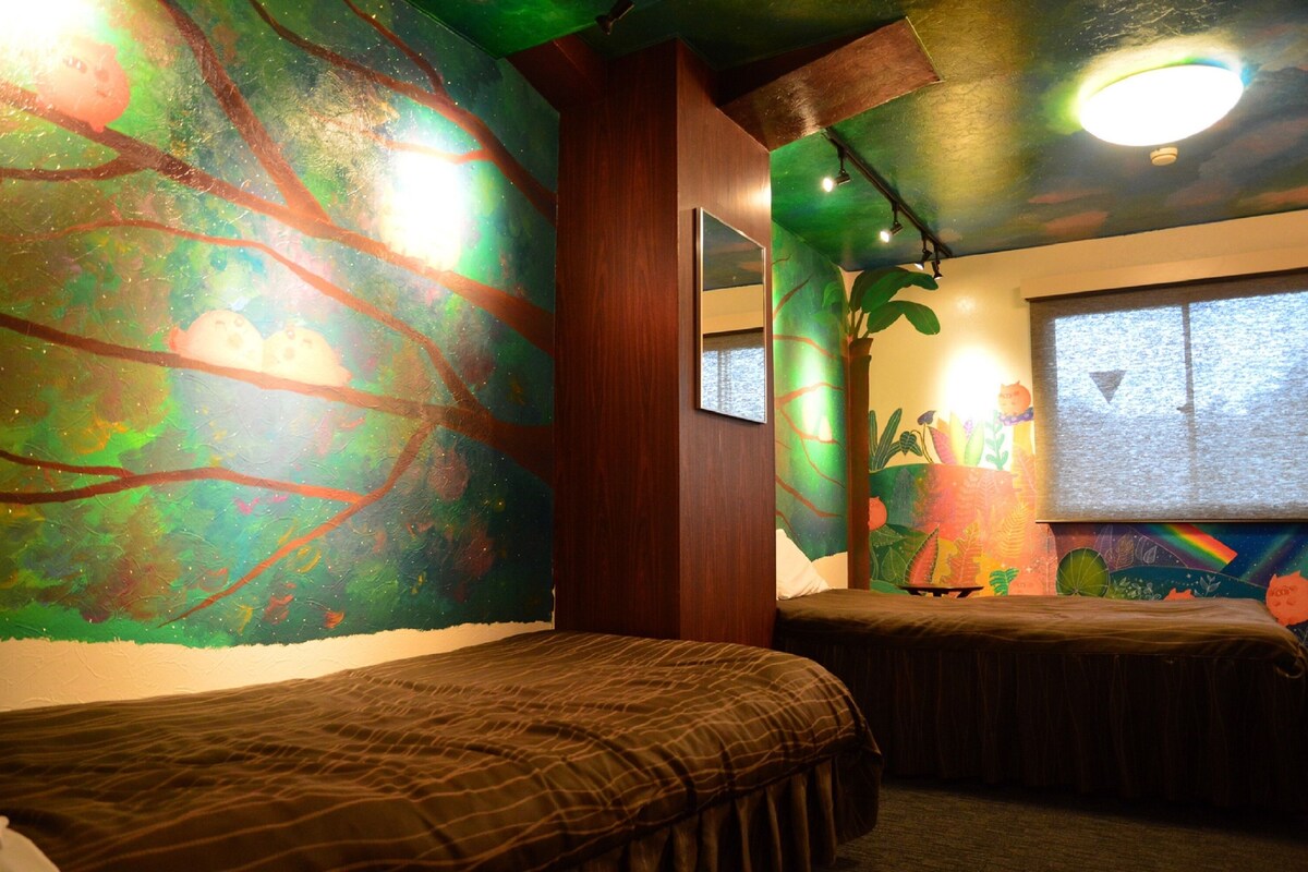 A room with two beds, a large window, and a wall mural.