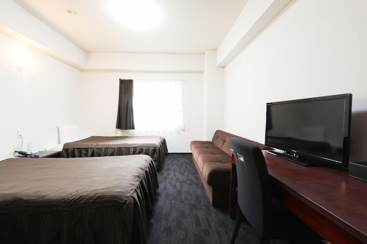 A hotel room with two beds, a sofa, a TV, and a window with curtains.