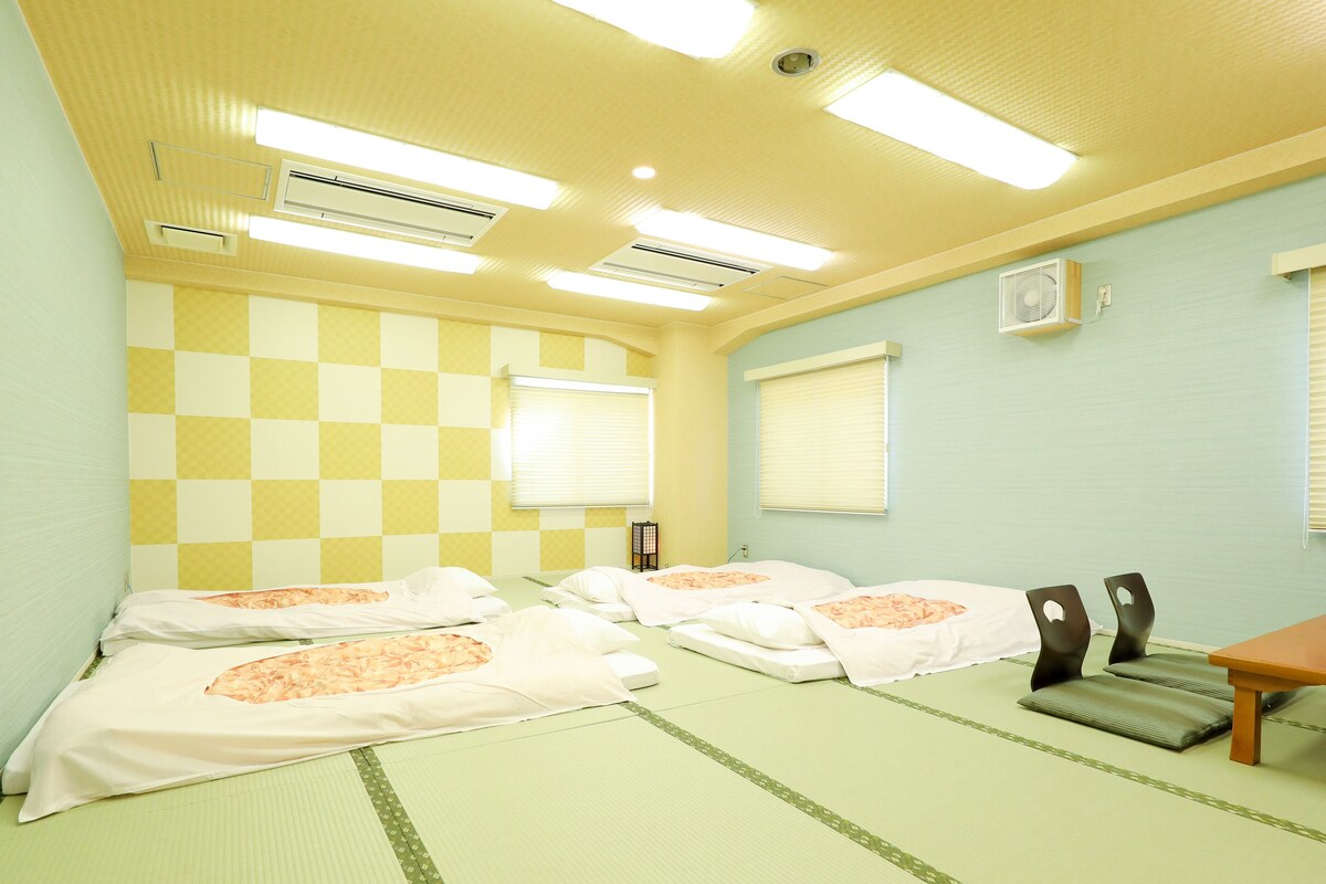 A hotel room with checkered walls, air conditioning units, a bed with floral bedding, a small table, and a chair.