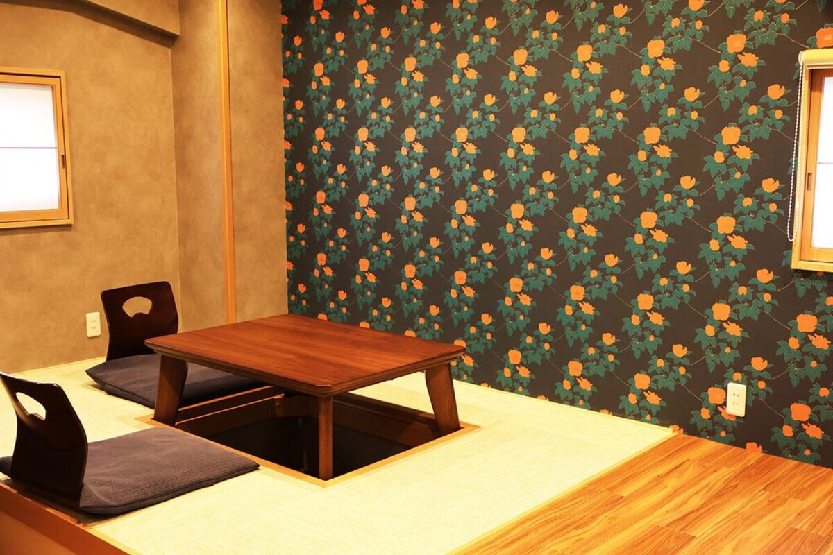 A room with a wooden table and chairs, a window, and a floral wallpaper.