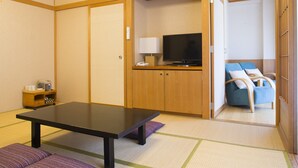 Een kamer met een tatami vloerkleed, een lage tafel, een televisie, een bank en een klein kastje met een waterkoker.