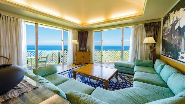 A room with a large window, a sofa, a coffee table, and a painting on the wall. - Southern links resort hotel (Yaese)