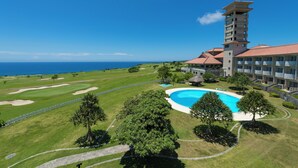 A golf course with a swimming pool, a tower, and a view of the ocean. - Southern links resort hotel (Yaese)
