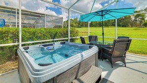 Ein Whirlpool mit Glastisch und -stühlen, einem blauen Sonnenschirm und Blick auf ein grünes Feld.