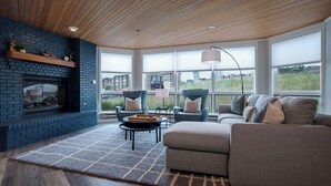 A modern living room with a brick fireplace, comfortable seating, and large windows offering a view of the outdoors. - CX113 | Onsite Check-In | Direct Access to Ski Area | Winter Shuttle | Hot Tub (Steamboat Springs)