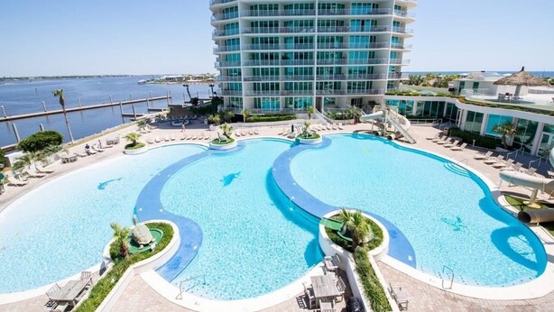 Ein Hotel mit großem Poolbereich, einem hohen Gebäude mit Balkonen und Blick auf das Meer.