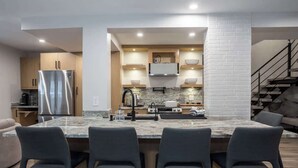 Une cuisine moderne dotée d’un îlot central, d’appareils électroménagers intégrés et d’un escalier menant à un autre niveau.