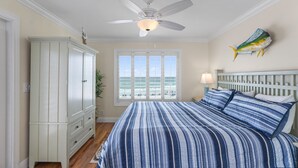 Ein Schlafzimmer mit Bett, Deckenventilator, Fenster mit Blick, Kleiderschrank und Nachttisch mit Lampe.