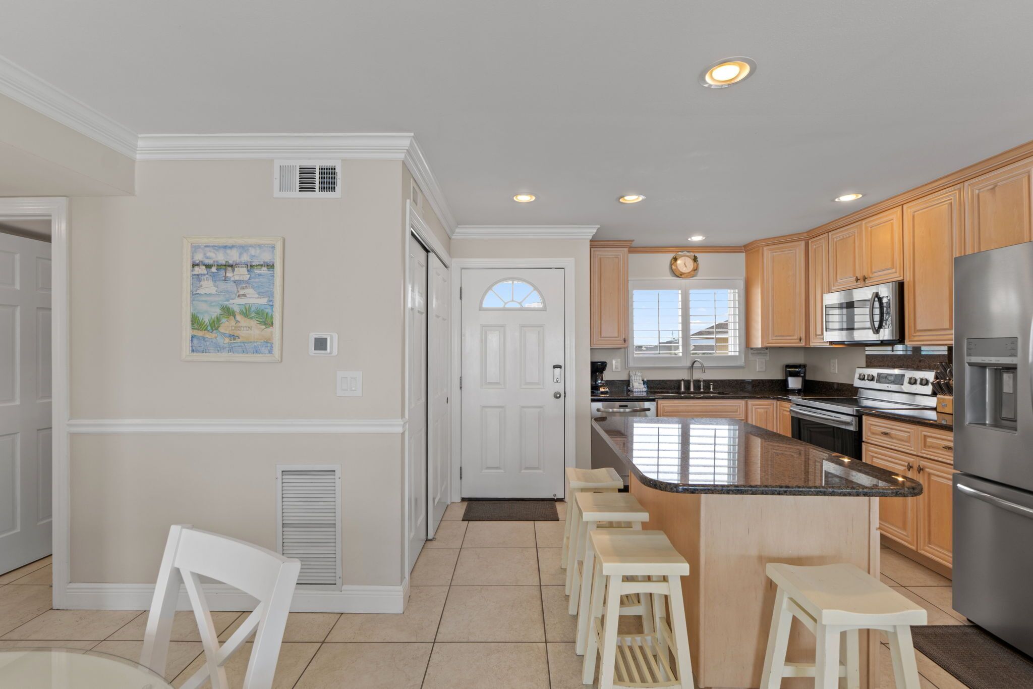 A kitchen with wooden cabinets, a stainless steel refrigerator, a microwave, a stove, and a large island with bar stools.