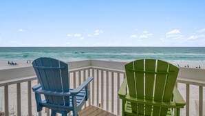Blick auf einen Strand mit zwei Adirondack-Stühlen auf einer Holzterrasse.