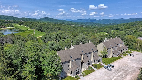 A large, multi-story building with a symmetrical roofline and multiple chimneys, surrounded by lush greenery and a golf course.