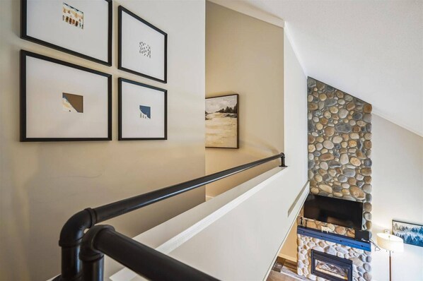 Loft Hallway - The open loft walkway adds extra space while overlooking the stone fireplace and living area.