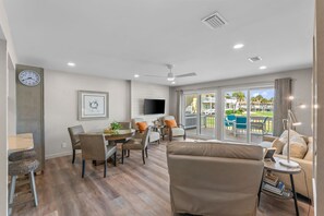 A modern living room with a dining area, a flat-screen TV, and a balcony with a view of the surroundings.