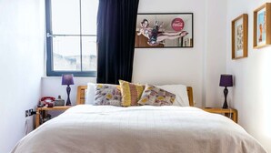 Cama bem arrumada com almofadas florais, um telefone antigo e um anúncio emoldurado de Coca-Cola na parede.