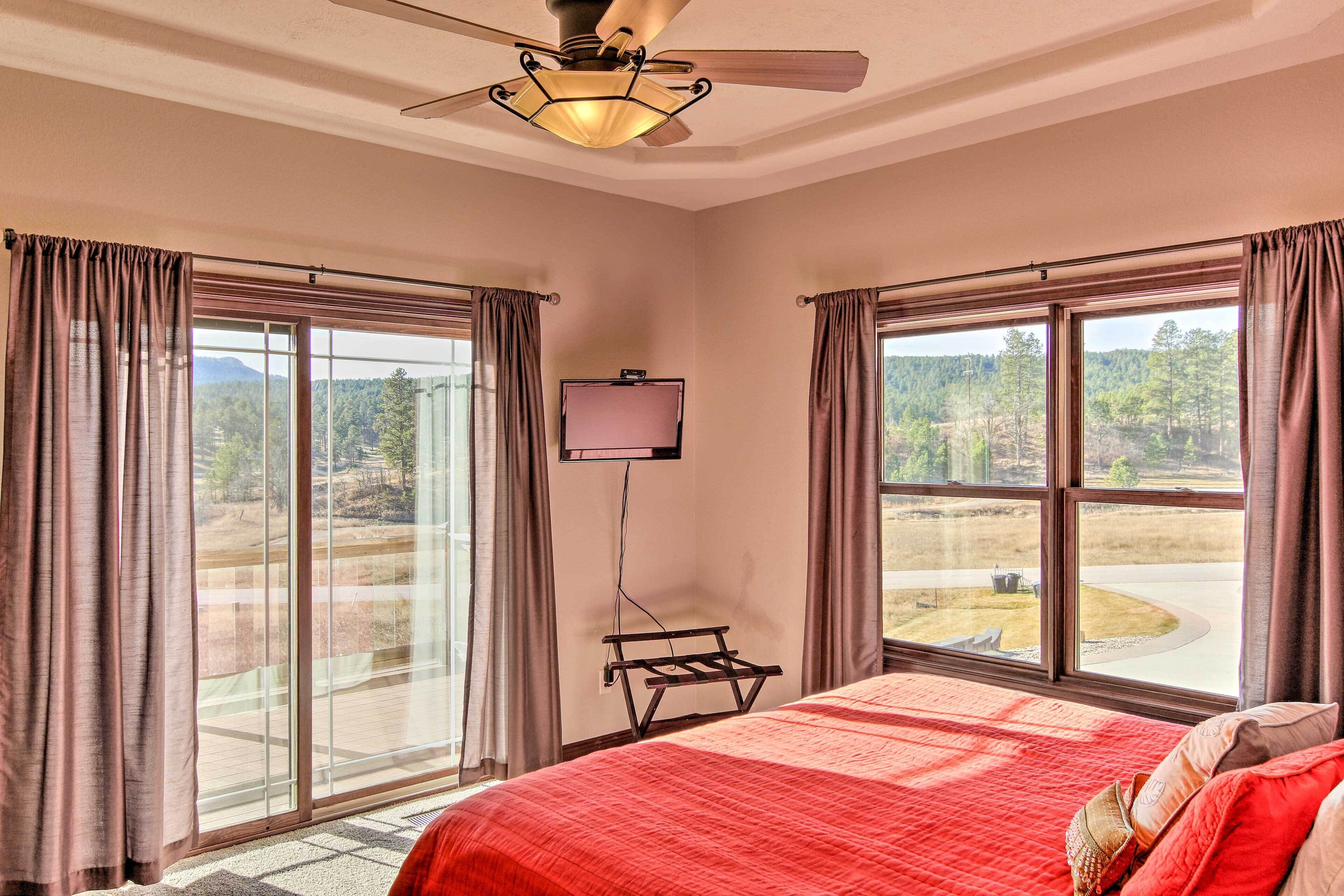 Ein Schlafzimmer mit einem großen Bett, einem Deckenventilator, einem Wand-Fernseher und großen Fenstern mit Vorhängen.