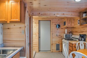 A compact kitchen with wooden walls, a microwave, stove, sink, and white chairs.