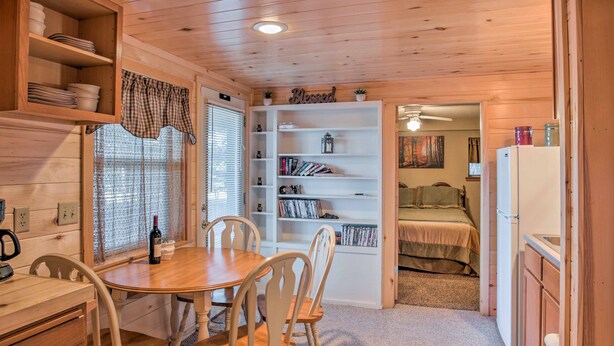 Interior acogedor de una cabaña con una mesa de comedor de madera, sillas, una estantería y una pequeña cocina.
