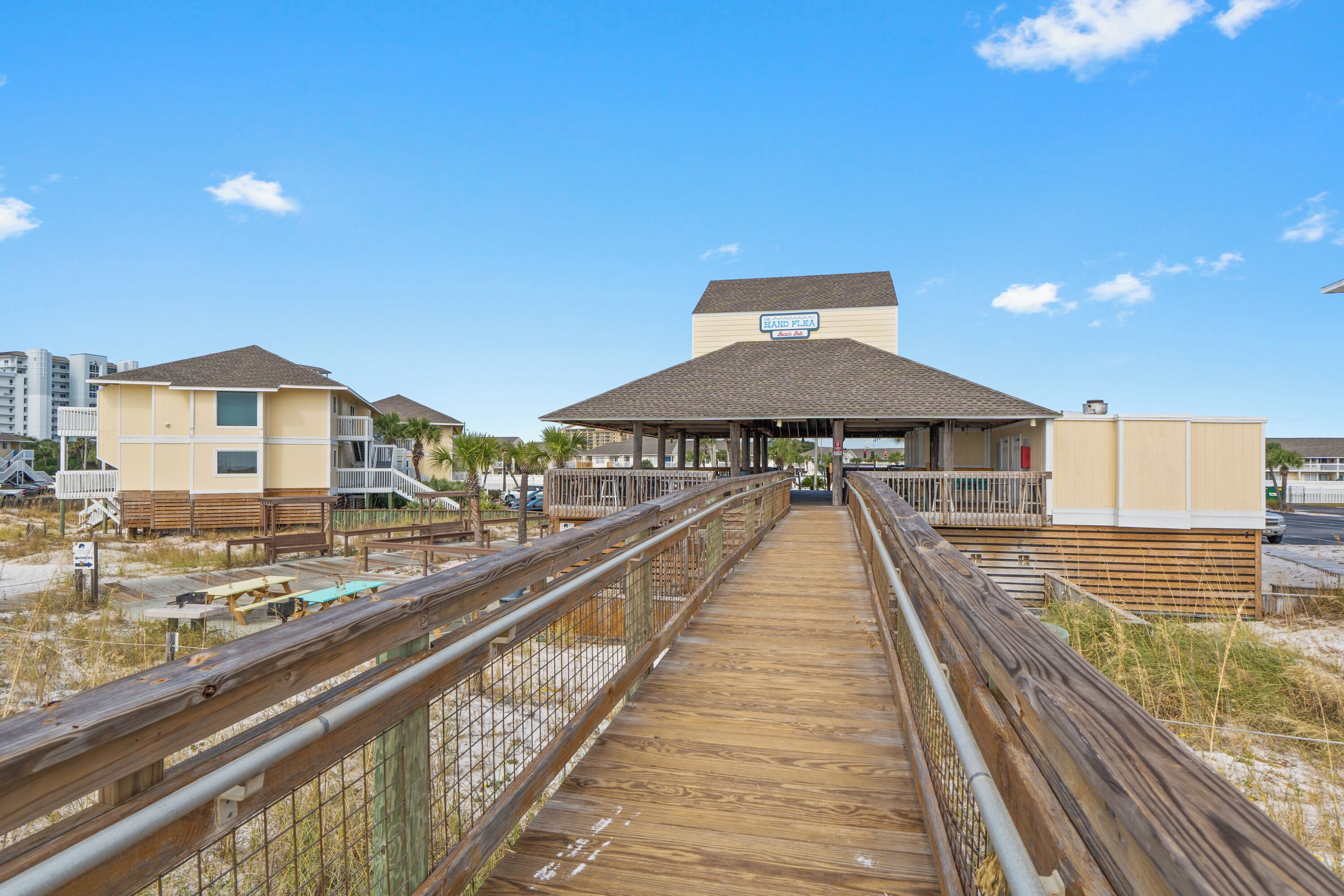 A wooden boardwalk leading to a building with a covered area and a sign that reads "BAJO PLATA."