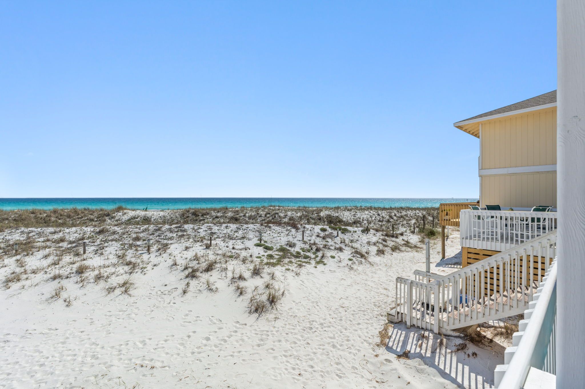 A beach view from a balcony with a wooden deck and white railing.