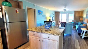 A kitchen with a stainless steel refrigerator, wooden cabinets, a granite countertop, and a dining area with a table and chairs. - Beachfront Stay with Amazing Views (Destin)