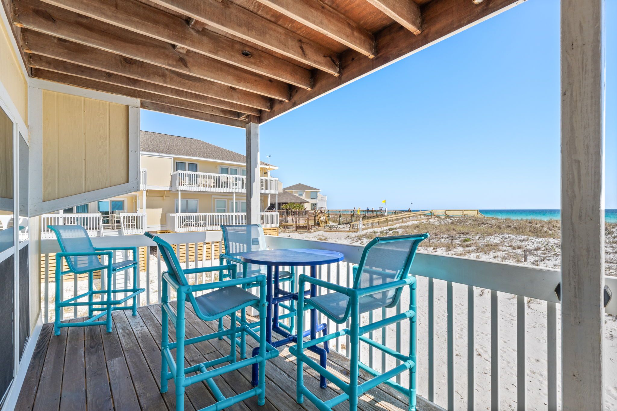 Une terrasse en bois avec des sièges extérieurs et une vue sur la plage et l’océan.