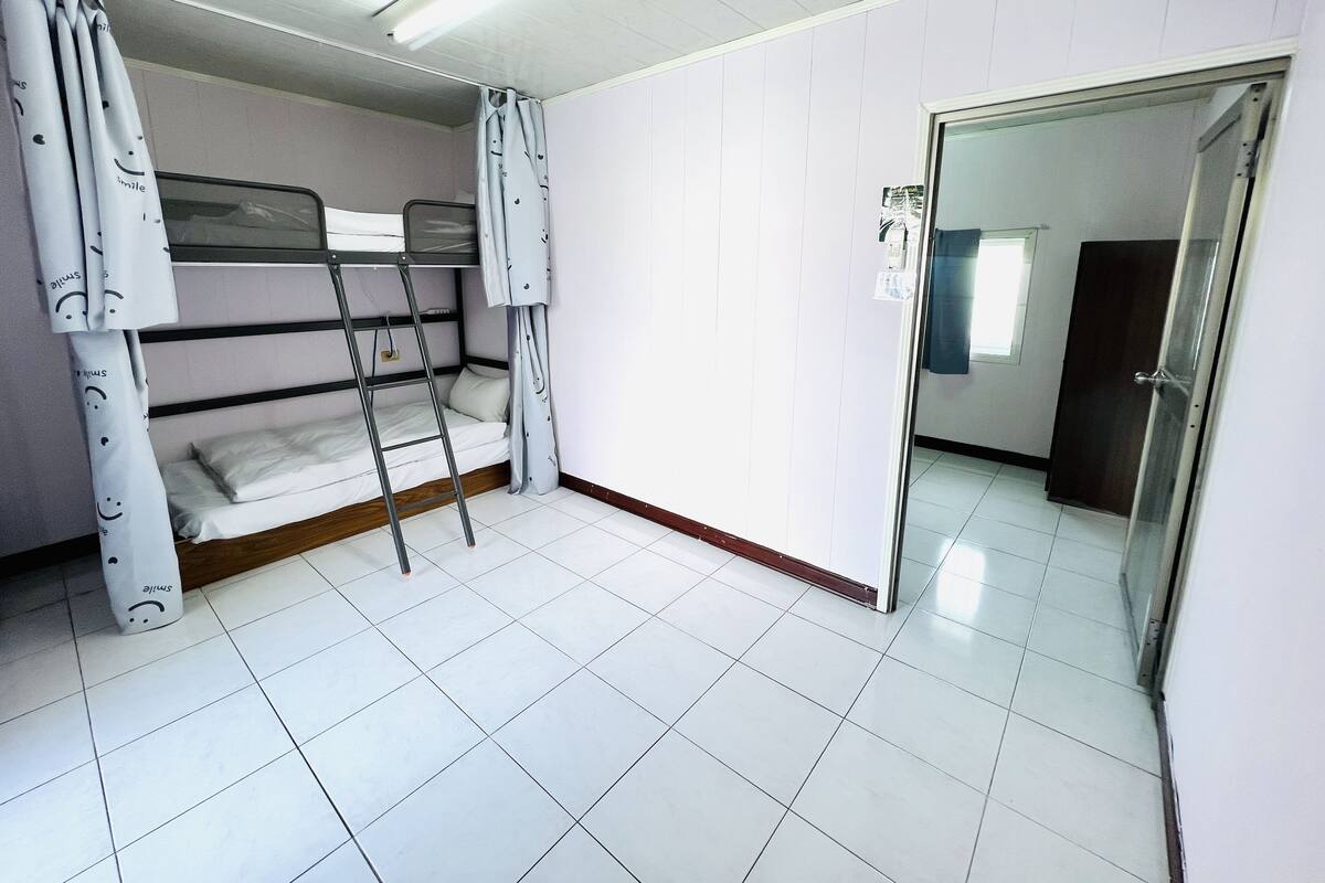 Un dormitorio con literas, una escalera y una puerta que da a otra habitación.