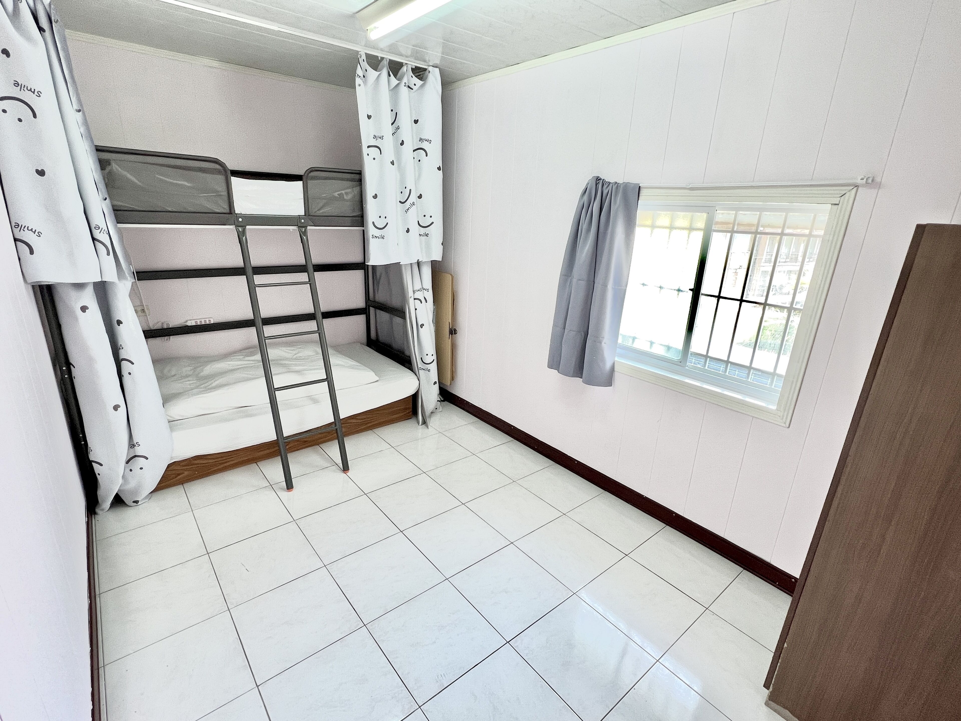 Een kamer met stapelbedden, een raam met gordijnen en een betegelde vloer.