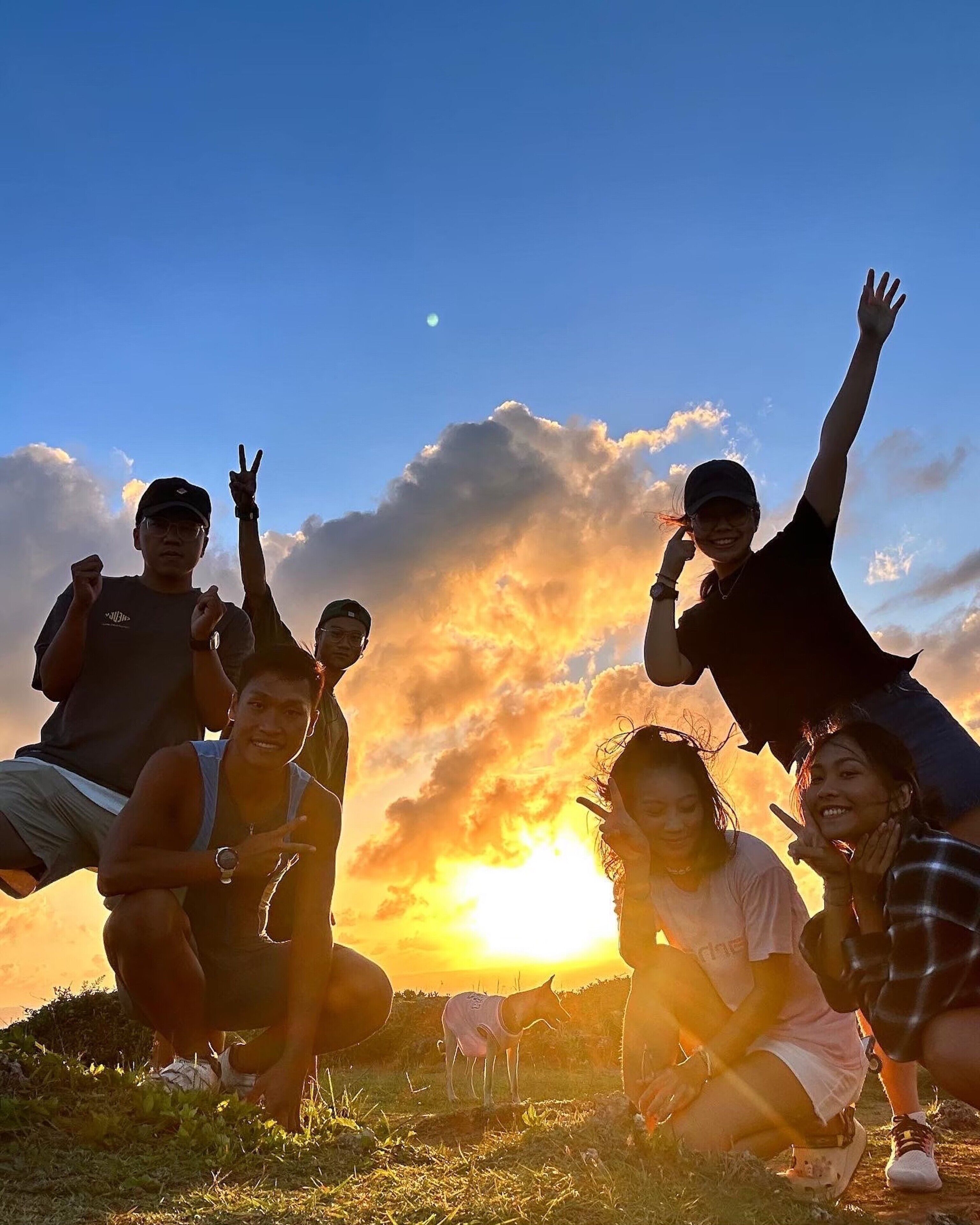 A group of people posing on a grassy field with a sunset in the background.