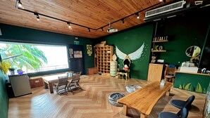 A cozy room with a wooden ceiling, a large window with a view of palm trees, a wooden table, two chairs, a bookshelf, and a decorative chair with wings. - 返璞歸真KO hostel 墾丁背包客棧 (Hengchun)