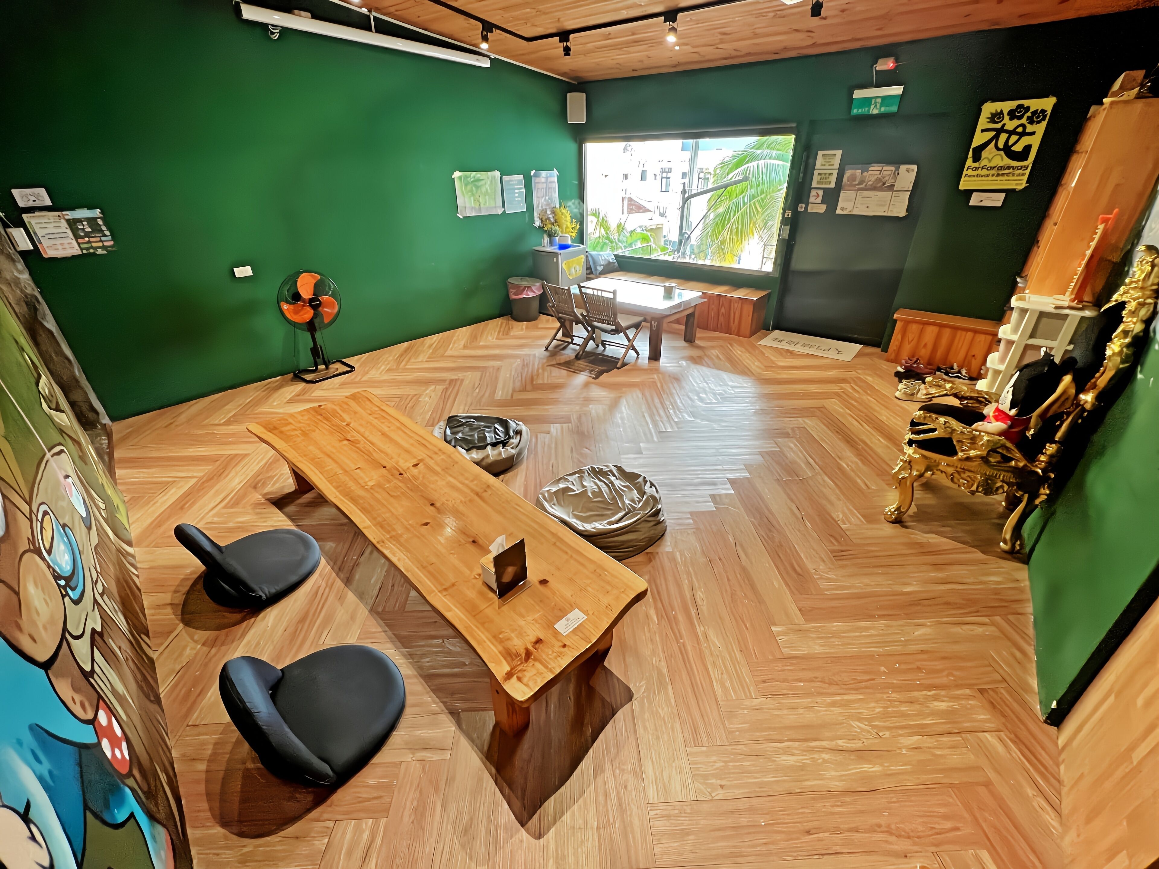 A room with a wooden table, two black chairs, a green wall, and a window with a view of buildings.