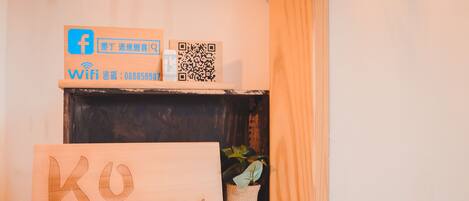A wooden shelf with a sign reading "KO" and a QR code, a small potted plant, and a couple of white bottles.
