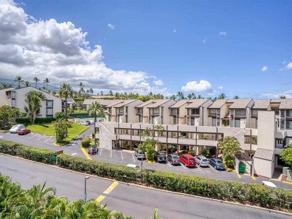 A hotel with a row of rooms, a parking lot, and a clear sky. - Island Chic w/Loft! AC, Lanai, Kitchen, WiFi, Flat Screens+Laundry–Kamaole Sands 9411 (KIHEI)