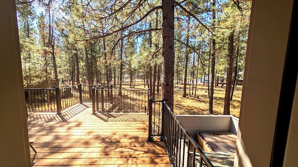 Enjoy the serene forest views from this spacious deck with a central staircase leading to an upper level.