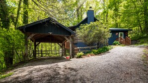 Un chalet rustique doté d’un porche abrité et d’une cheminée, entouré d’une forêt dense.