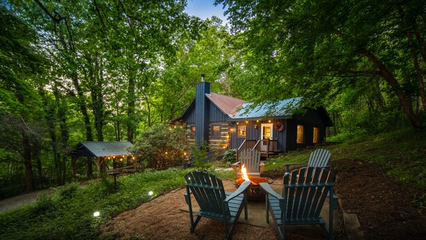 Un chalet rustique avec un foyer et des fauteuils Adirondack, situé dans un cadre forestier.