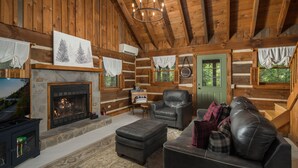 L’intérieur d’une cabane en rondins, avec une cheminée en pierre, des meubles en cuir et un lustre.