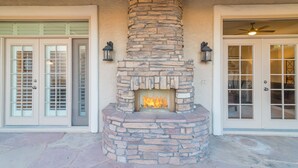 A stone fireplace with a fire, flanked by two doors with glass panels and exterior lighting fixtures. - A Beauty in Scottsdale! (Scottsdale)