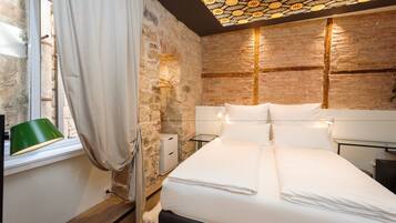 Un dormitorio con pared de piedra, una cama con ropa blanca, una lámpara verde y un accesorio de iluminación en el techo.