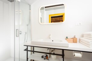 A modern bathroom with a glass shower enclosure, a white sink with a black frame, a mirror with a gold frame, and a stack of white towels. - Luxury Rooms Bajamonti (Split)