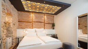 Ein modernes Schlafzimmer mit Backsteinwand, großem Bett, Nachttischen, einem Spiegel und einer besonderen Deckenleuchte.