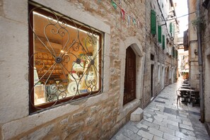 A narrow street with stone buildings, a window with decorative ironwork, and a row of tables and chairs outside a shop. - Luxury Rooms Bajamonti (Split)