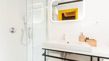 Un baño moderno con cabina de ducha de vidrio, un lavabo blanco con tocador de madera y un espejo con marco amarillo.