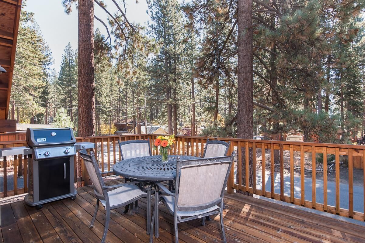 A wooden deck with a grill, chairs, and a table with a vase of flowers.